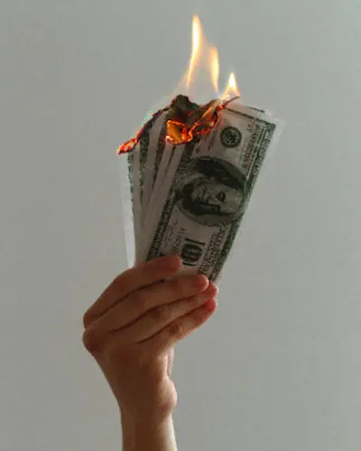 Parkinson's Law Article - money held in hand being burned. Money wasted is human tendency. Overcome and maximize financial control.